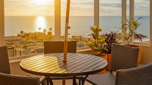 Un balcon avec une table ronde et des chaises, d’où l’on peut admirer le paysage urbain de la côte au coucher du soleil.