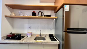 Une cuisine équipée d’un réfrigérateur en acier inoxydable, d’une cuisinière, d’un évier et d’une étagère en bois au-dessus du plan de travail.
