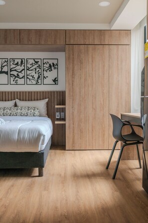 Une chambre à coucher avec un lit, un bureau et une chaise. Des œuvres d’art sont accrochées au mur au-dessus du lit.