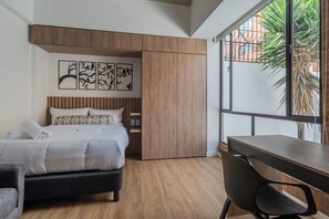A bedroom with a bed, a desk, and a window with a view of greenery. - Apto en Sierra Madre 208 (Bogotá)