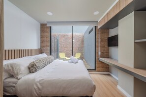 Une chambre moderne avec un grand lit, un téléviseur fixé au mur et une porte-fenêtre coulissante donnant sur un espace extérieur.