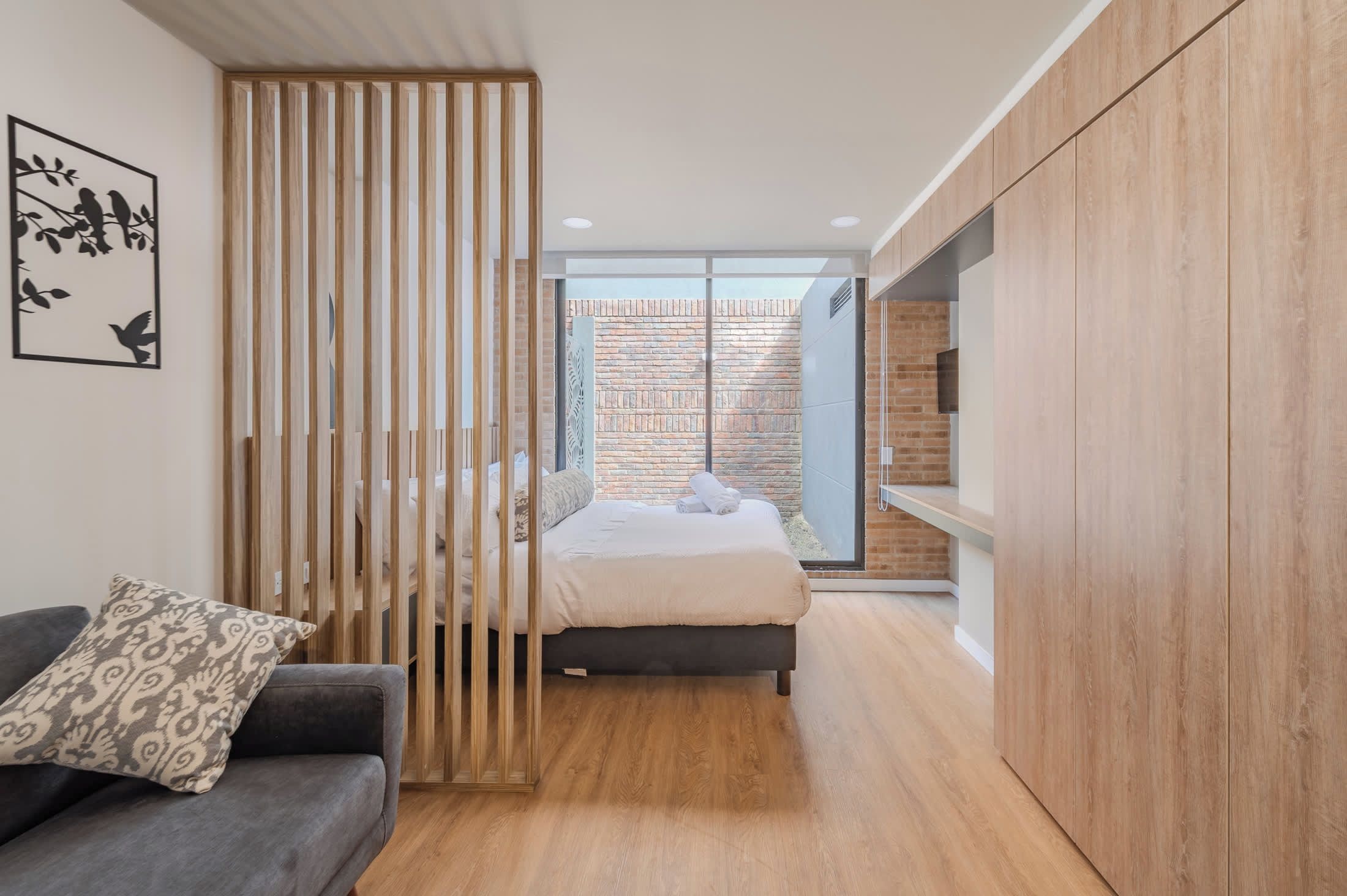 A modern bedroom with a bed, a wooden wardrobe, a grey sofa, and a decorative panel with bird silhouettes.