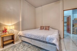 A bedroom with a bed, a nightstand with a lamp, and a small table with a vase of flowers. - Haze Villa | Tropical Retreat & Pool (Puerto Viejo De Talamanca)