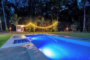 A swimming pool with a tiled edge, surrounded by a grassy area and trees. - Kush Villa | Caribbean Hideaway & Pool (Puerto Viejo de Talamanca)