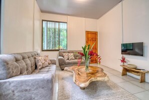 A living room with a sofa set, a coffee table, a TV, and a wooden door. - Kush Villa | Caribbean Hideaway & Pool (Puerto Viejo de Talamanca)