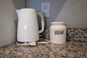 Een witte waterkoker en een witte suikerpot op een granieten aanrecht.