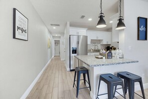 Een moderne keuken met een centraal eiland, barkrukken en een bord met de tekst 'Eat Drink Thankful'.