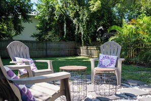 Eine Terrasse mit zwei Adirondack-Stühlen, einem kleinen runden Tisch und einem Zierkissen.