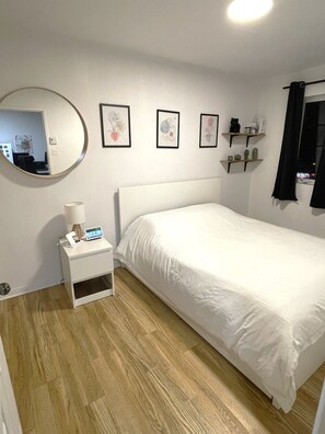 Ein Schlafzimmer mit einem Bett, einem Nachttisch mit Lampe, einem Spiegel und gerahmten Pflanzenbildern an der Wand.