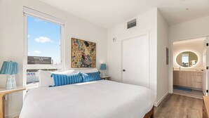 A bedroom with a large bed, a window, a painting, a door, and a bathroom with a mirror. - Light-Filled K-town 3BD 3BTH W/Pool, Gym & Parking (Los Angeles)