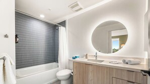 A modern bathroom with a bathtub, toilet, and vanity with a mirror. - Light-Filled K-town 3BD 3BTH W/Pool, Gym & Parking (Los Angeles)
