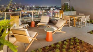 A rooftop terrace with seating arrangements, a dining table, and a view of the cityscape at night. - Light-Filled K-town 3BD 3BTH W/Pool, Gym & Parking (Los Angeles)