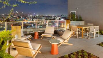Eine Dachterrasse mit Sitzgelegenheiten, einem Esstisch und Blick auf die nächtliche Skyline.