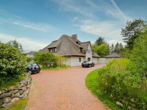 Ein Haus mit einem Strohdach, einem gepflasterten Einfahrtsweg und einer Steinmauer an einer Seite.