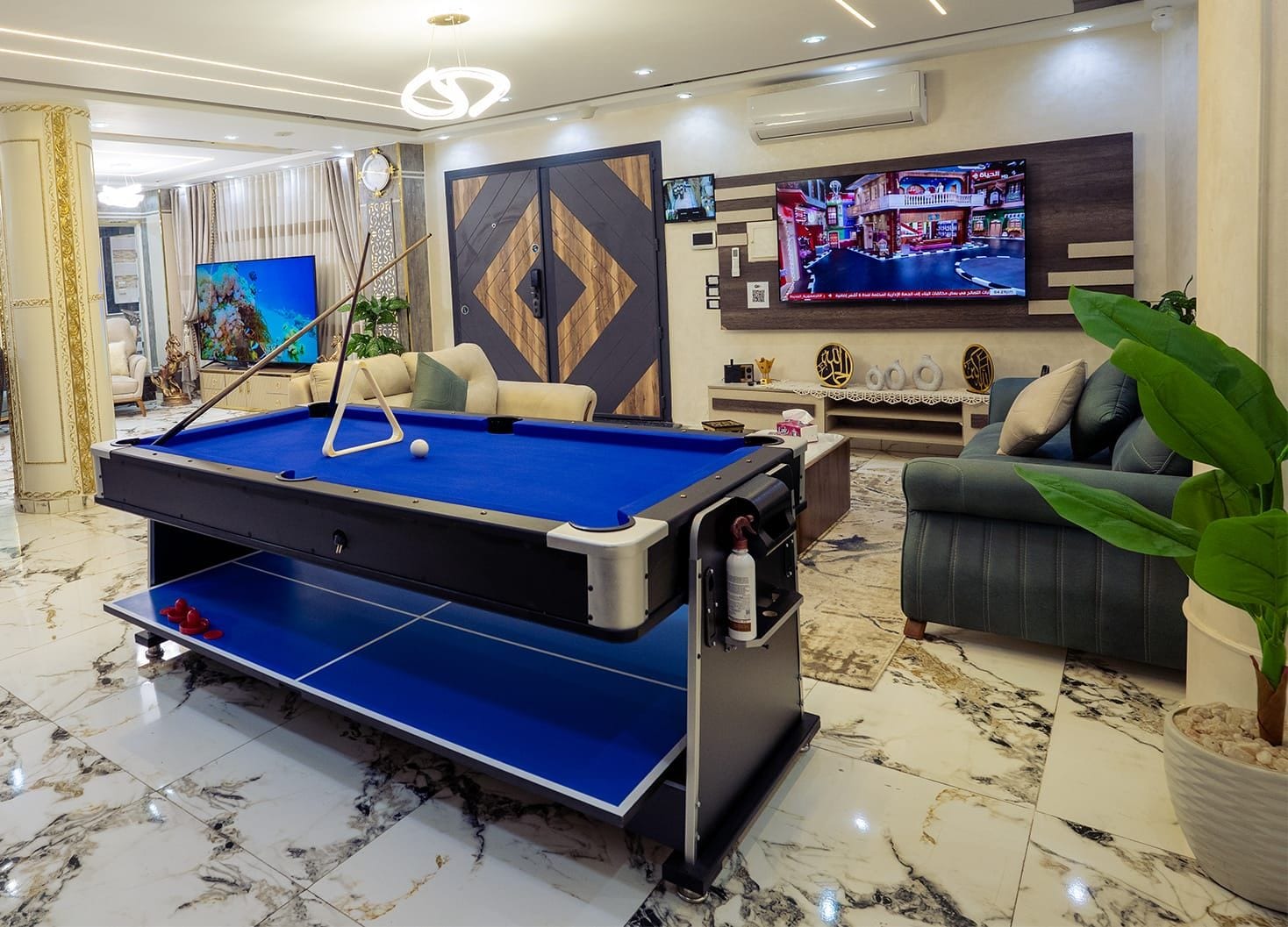 A pool table in a well-lit room with a sofa and a television.