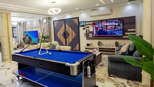 Een biljarttafel in een goed verlichte kamer met een bank en een televisie.