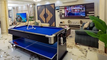 A pool table in a well-lit room with a sofa and a television.