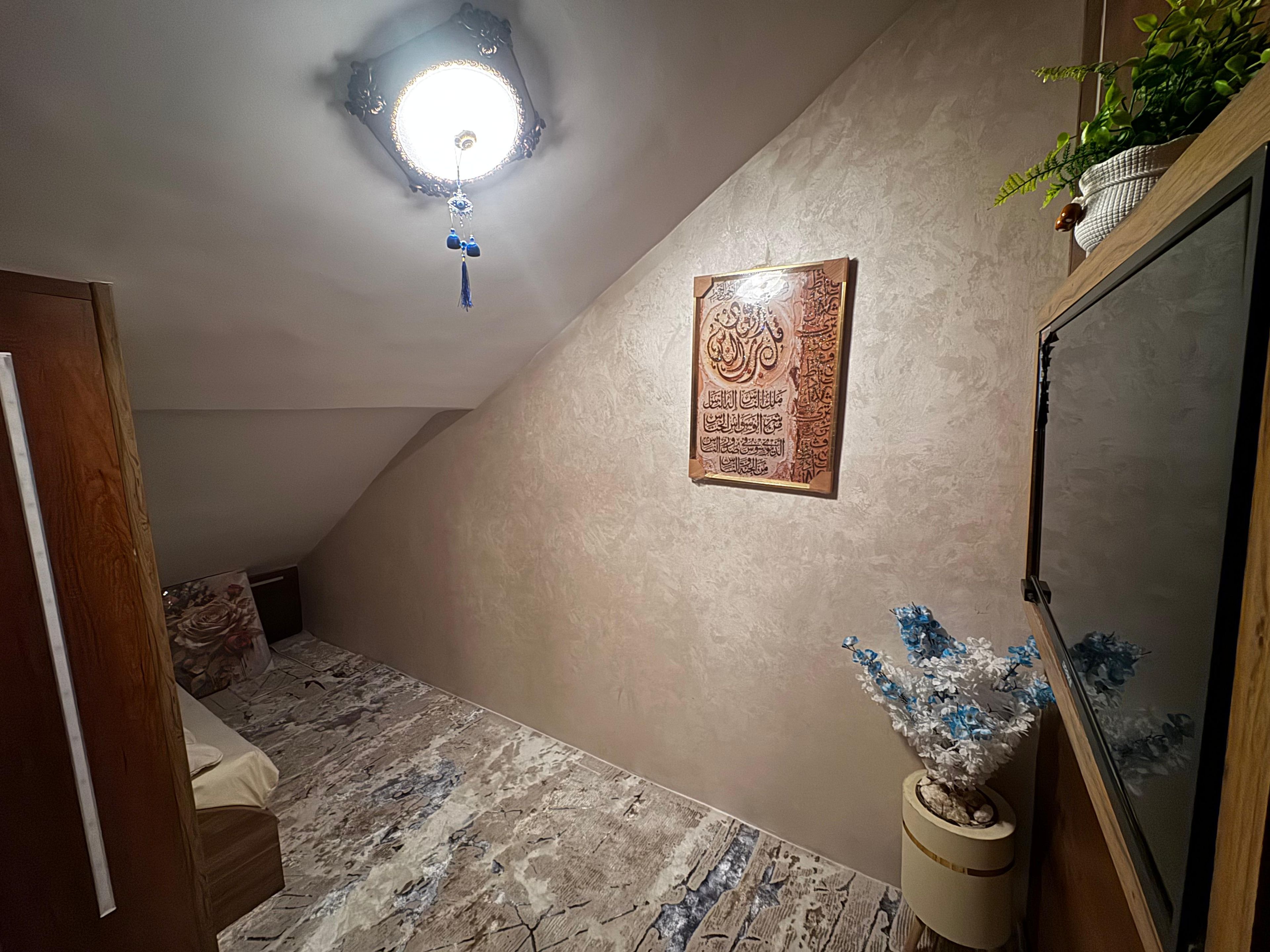 Une pièce avec un plafond en pente, un luminaire décoratif, une œuvre calligraphique encadrée, une petite plante et un miroir.