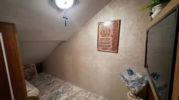 Una stanza con soffitto spiovente, un lampadario decorativo, un'opera calligrafica incorniciata, una piccola pianta e uno specchio.