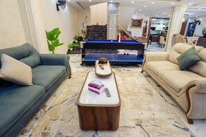 A living room with a pool table, two sofas, a coffee table, and a staircase leading to an upper level.