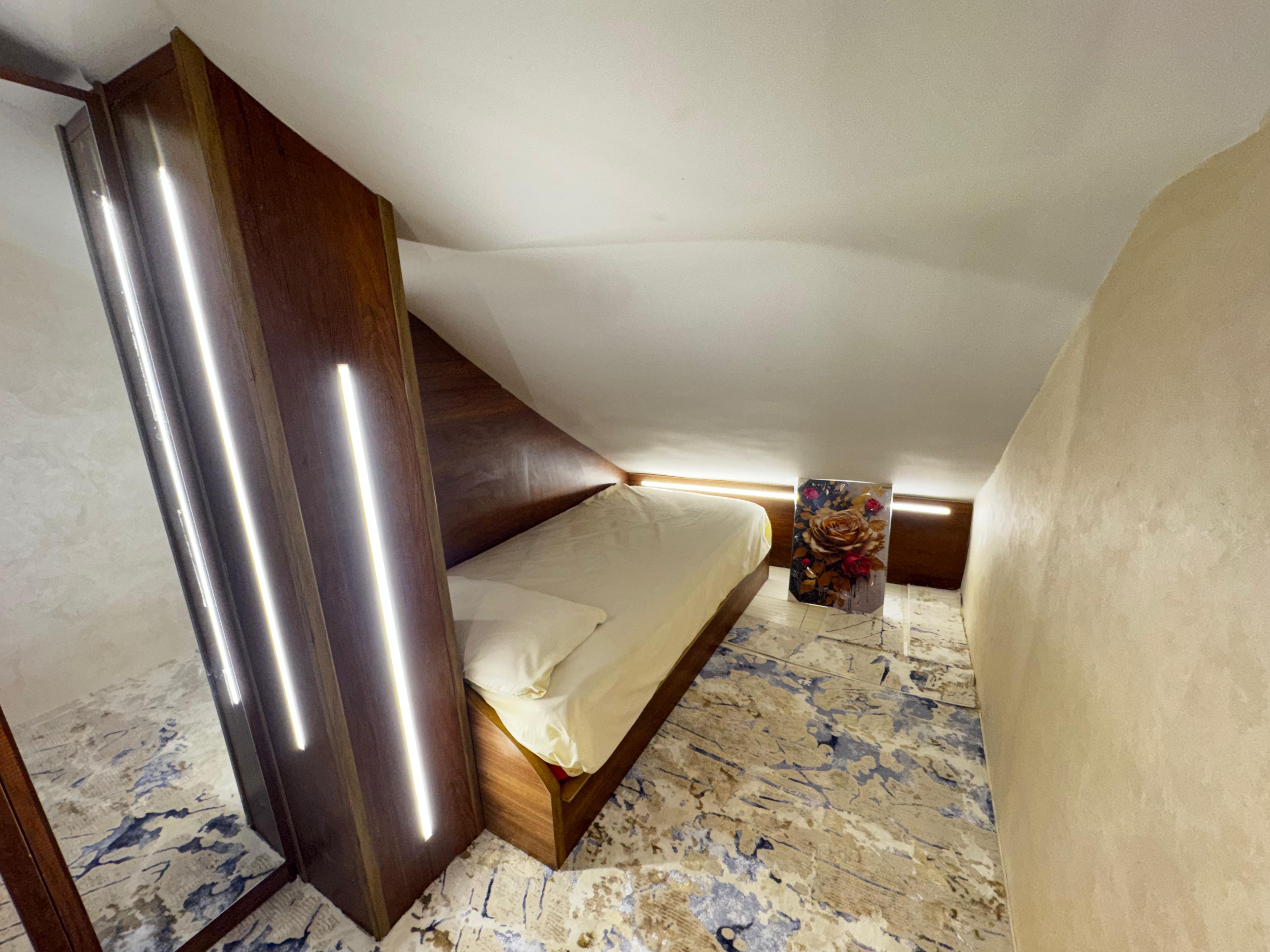 Une chambre à coucher avec un lit, une tête de lit en bois et une table de chevet ornée d’un objet à motifs floraux.