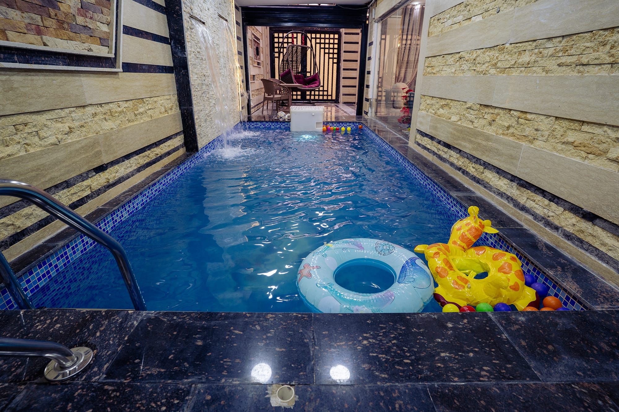 A swimming pool with a water feature, a lounge chair, and inflatable toys.