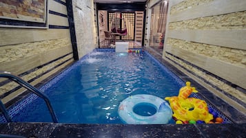 A swimming pool with a water feature, a lounge chair, and inflatable toys.