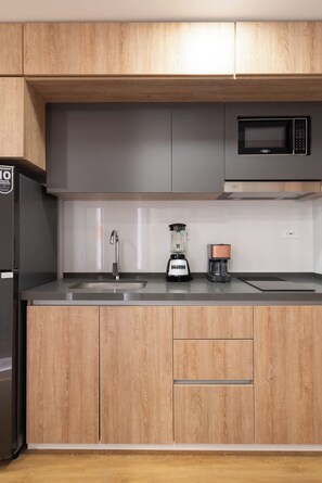 Eine Küche mit Holzausstattung, einer Edelstahlspüle, einem schwarzen Kühlschrank, einer Mikrowelle, einem Mixer und einer Kaffeemaschine.