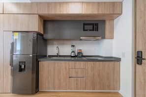 Een moderne keuken met een roestvrijstalen koelkast, een magnetron, een koffiezetapparaat en houten keukenkastjes.