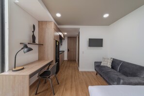 Ein moderner Wohnraum mit Schreibtisch, Stuhl, Sofa und einem an der Wand befestigten Fernseher.