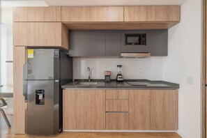 Eine moderne Küche mit Holzschränken, einem Edelstahlkühlschrank, einer Mikrowelle und einer Kaffeemaschine.