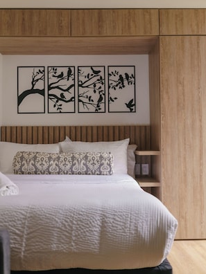 A bedroom with a bed, pillows, a bedside table, and a wall-mounted artwork of birds on branches. - Studio Bogota 1Bed Sierra Madre 106 (Bogotá)