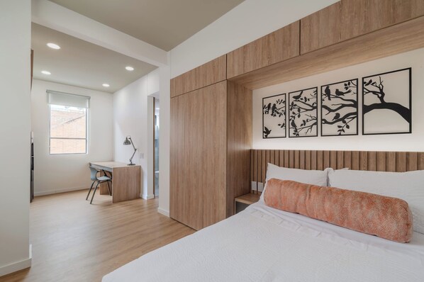 Un dormitorio moderno con cabecera de madera, cama con ropa de cama blanca, escritorio con silla y decoración en la pared.