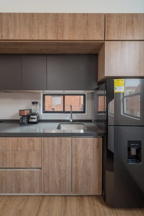 A kitchen with wooden cabinets, a stainless steel sink, a refrigerator, and a window. - Studio Bogota 1Bed Sierra Madre 306 (Bogotá)