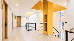 A hallway with a wooden door, a staircase with a yellow accent, and a tiled floor. - Apto 1 Hab Ed sierra Madre 209 (Bogotá)