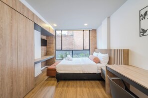 A modern bedroom with a bed, a bench, a desk, and a view of the outside. - Apto 1 Hab Ed sierra Madre 209 (Bogotá)