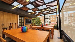 A modern interior with wooden tables and chairs, a large window with a view of buildings, and a ceiling with wooden slats and lights. - Studio Moderno Bogota 1bed (Bogotá)