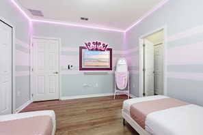 A bedroom with two beds, a vanity with a mirror, a television on the wall, and a decorative crown above it. - Grand Villa w Pool, Spa, Games & Theatre near Disney (Davenport)