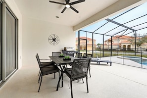 A covered patio with a dining table and chairs, a grill, and a pool view. - Grand Villa w Pool, Spa, Games & Theatre near Disney (Davenport)
