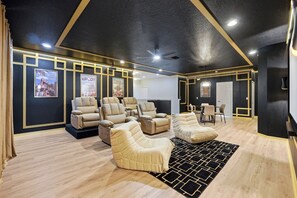 A room with a ceiling fan, reclining chairs, a dining table with chairs, and posters on the wall. - Grand Villa w Pool, Spa, Games & Theatre near Disney (Davenport)
