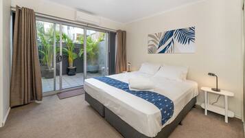 A bedroom with a bed, a bedside table, a window with curtains, and a view of the outside.