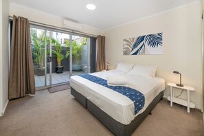 A bedroom with a bed, a bedside table, a window with curtains, and a view of the outside. - Unbeatable Convenience, the City on your Doorstep (Fortitude Valley)