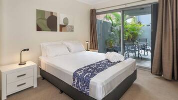 A hotel room with a bed, a nightstand, a lamp, a sliding glass door to an outdoor area with a table and chairs, and artwork on the wall.