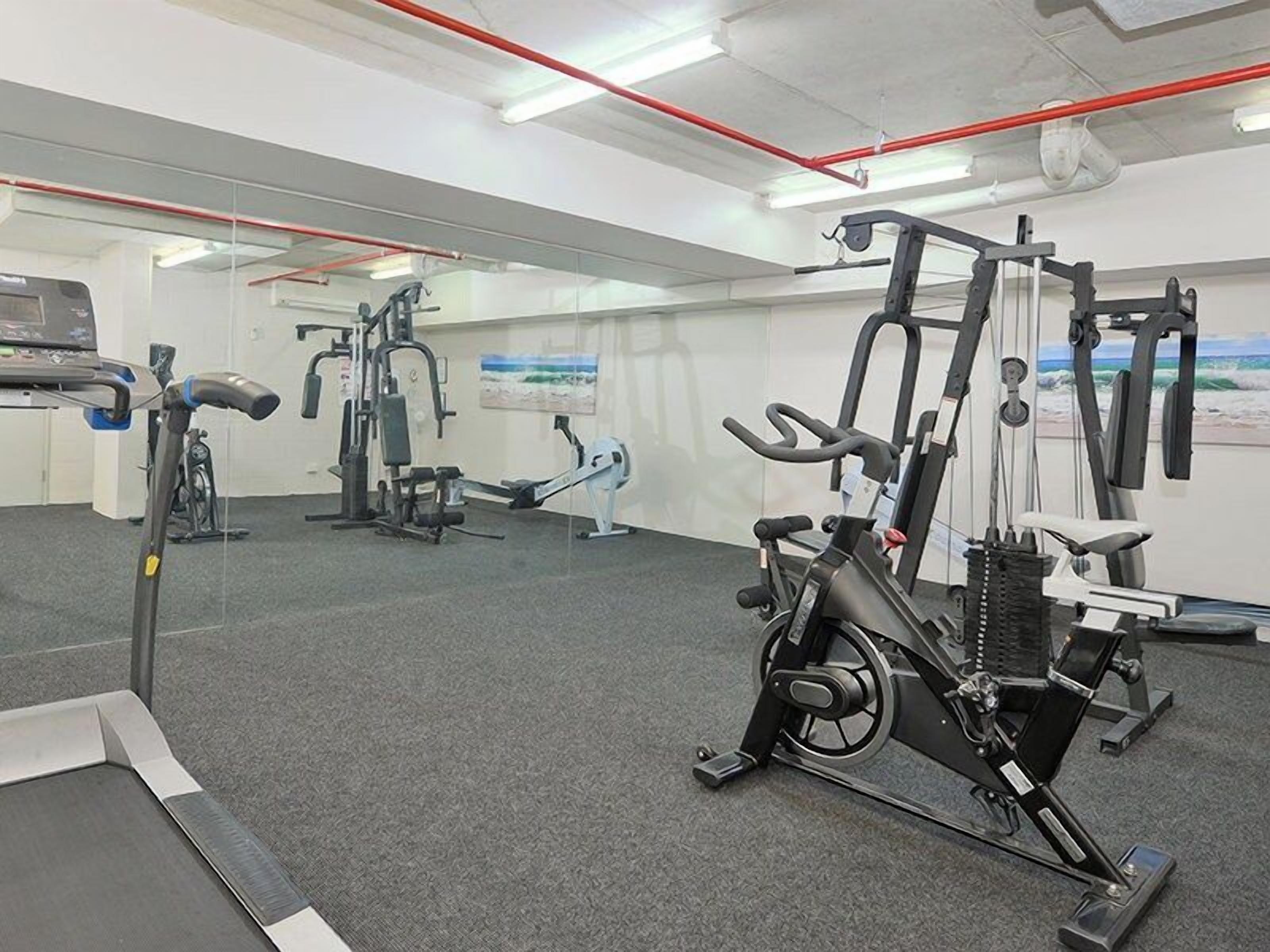 A gym with cardio machines, weightlifting equipment, and a mirrored wall.