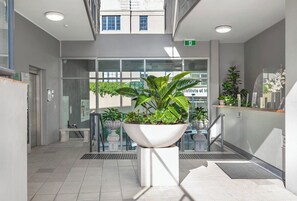 Un espacio interior moderno con una zona de recepción, un gran macetero con vegetación y una escalera que conduce a un nivel superior.