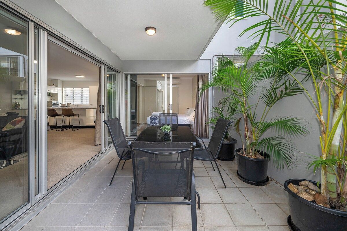 A modern room with a glass partition, a dining table with chairs, and potted plants.