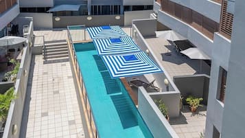 A rooftop swimming pool with blue and white striped umbrellas, surrounded by modern buildings.