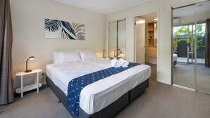 Ein Hotelzimmer mit Bett, Nachttisch, Lampe und Blick durch eine Schiebetür auf einen Außenbereich.