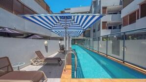 Ein Poolbereich auf dem Dach mit Liegestühlen, einem Pool und einer Glasrelung.