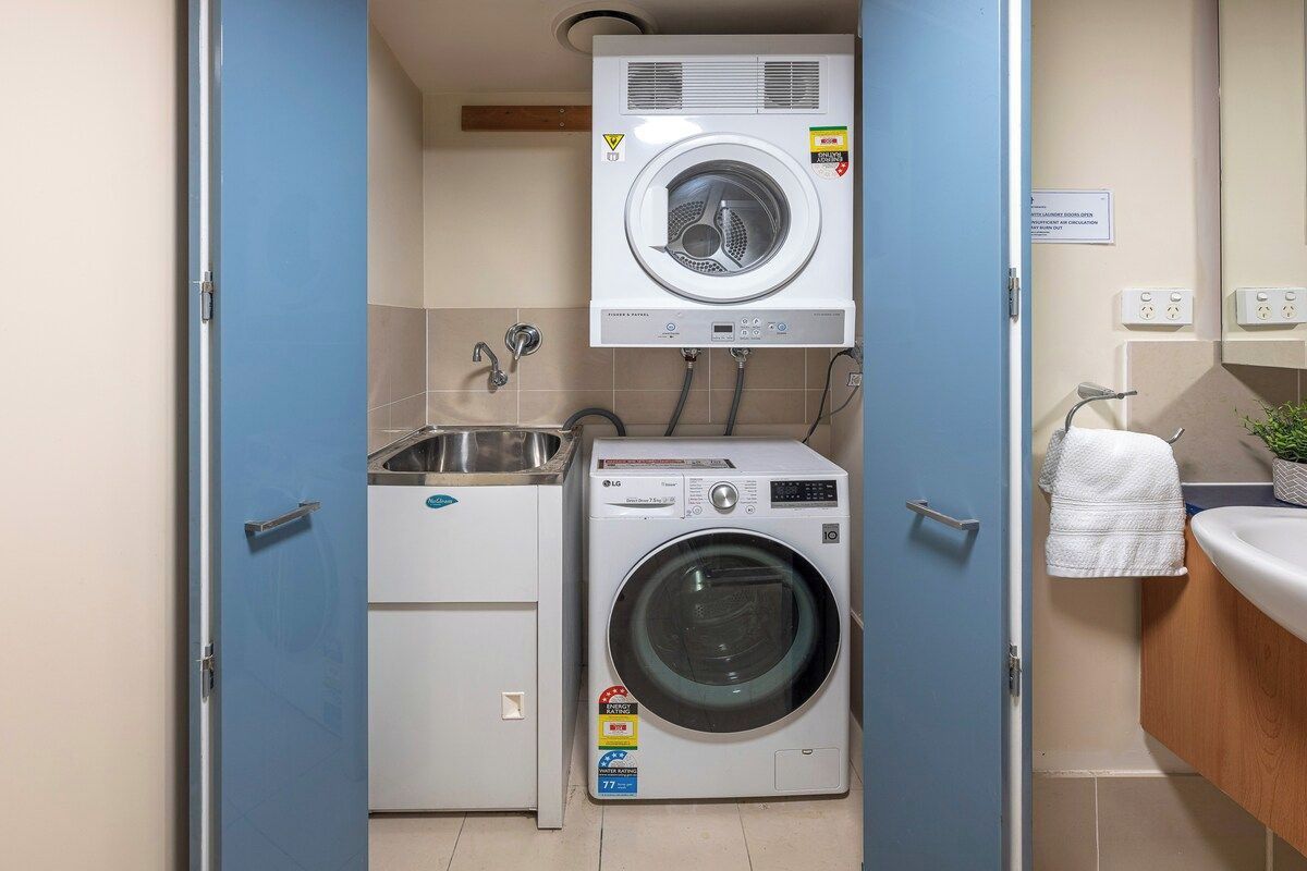 A compact laundry area with a front-loading washing machine and dryer, a sink, and a towel rack.